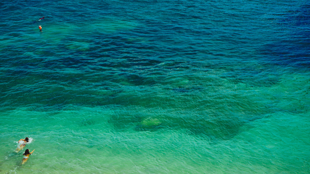 An areas view into pristine, shallow ocean waters. Gorgeous colors of tourqoise to deep blue are captured. Two swimmers are at the bottom left.